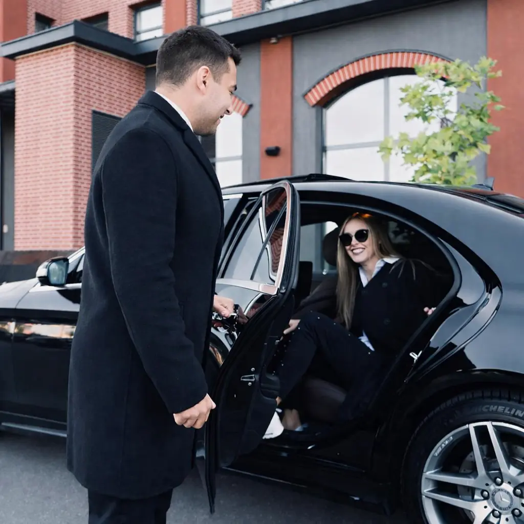 Chauffeur opening car door for smiling passenger during private transfer in Exeter